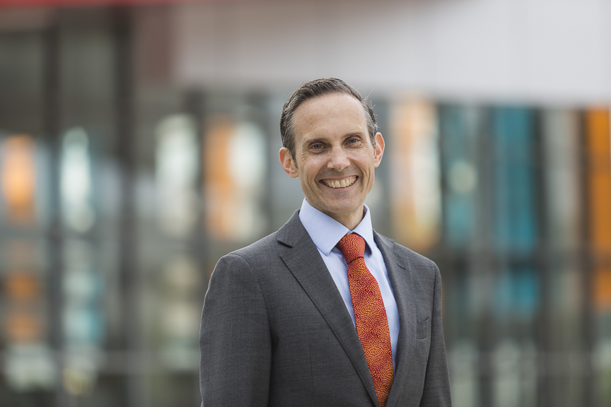 A photo of Andrew Leigh MP, wearing a suit and tie, smiling at the camera